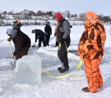 Three team members prepare to move a large block of ice onto a nearby tarp.